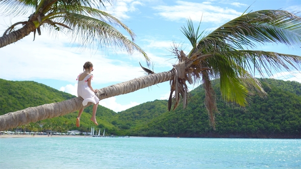 Adorable Little Girl at Tropical Beach Sitting on Palm Tree During Summer Vacation