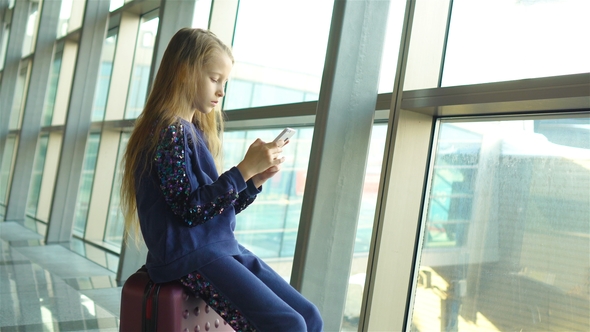 Adorable Little Girl in Airport Near Big Window Indoor Playing with Smartphone