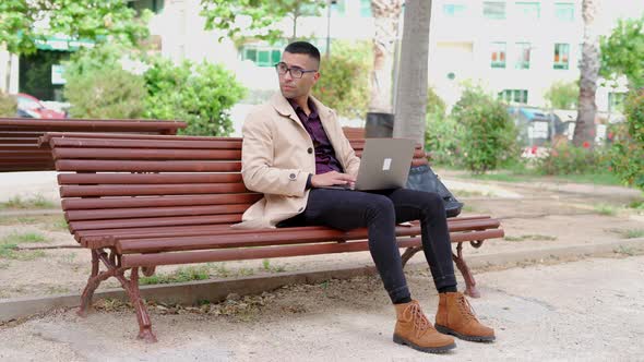 Young businessman in trendy outfit speaking on phone on bench