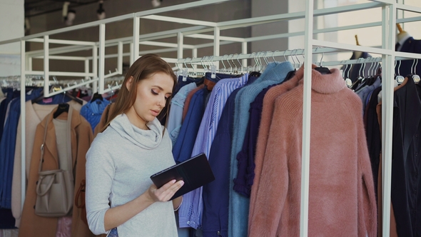 Young Businesswoman Is Checking Clothes in Her Store with Tablet in Hands