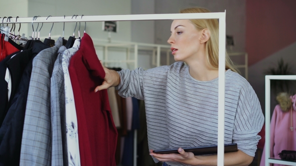 Young Businesswoman Is Checking Garments on Rails and Working with Tablet in Her Clothing Shop