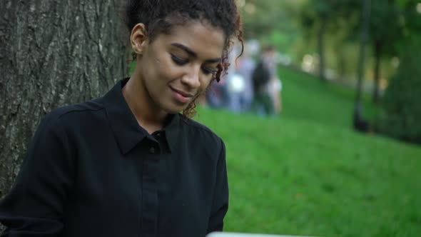 Closeup Happy Curly Afroamerican Girl in Black Dress with Makeup on Working on Laptop Laying on