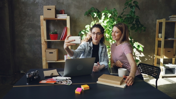 Young Businesswomen Are Making Selfie Together in Modern Office While Sitting at Desk