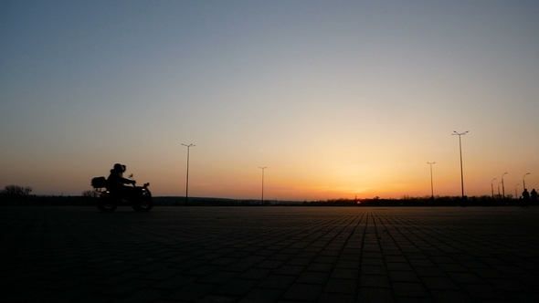 The Biker Rides on Quad Bike Over a Large Square Against the Backdrop of a Beautiful Sunset