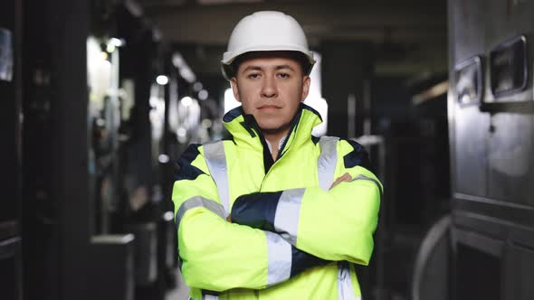 Confident Engineer Wearing Safety Vest and Hard Hat Crossing Arms at Electrical Control Room