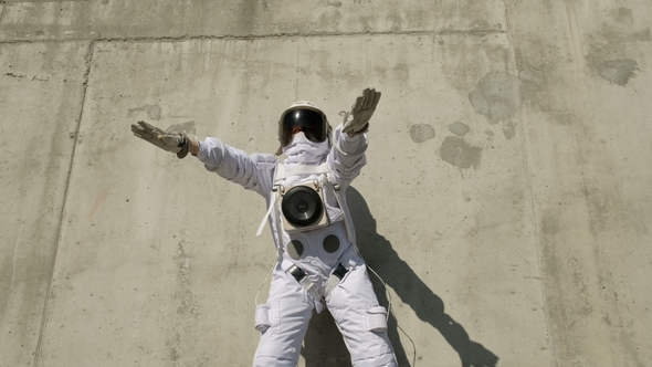 Funny Astronaut Makes Dancing against a Background of a Concrete Wall
