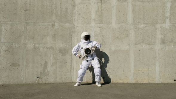 Funny Astronaut Makes Dancing. Against a Background of a Concrete Wall.