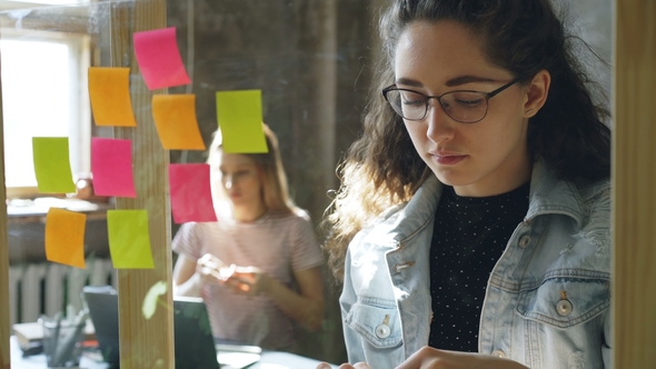 Shot of Attractive Young Businesswoman Standing and Sticking Colourful Memos on Glass Board. Her