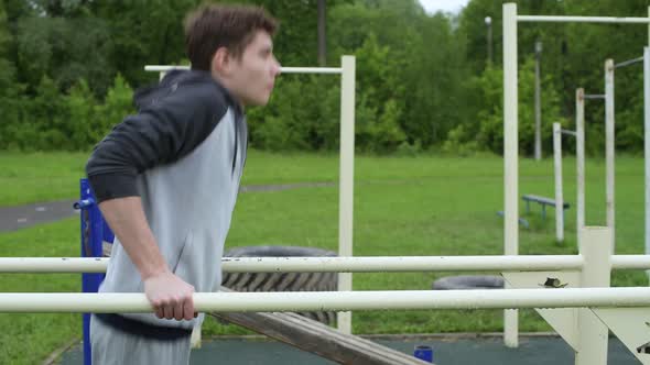 Side view of a training guy. teenager push ups on uneven bars