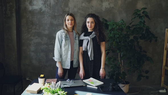 Two Young Female Business Colleagues Are Standing Together in Loft Style Office, Posing and Looking