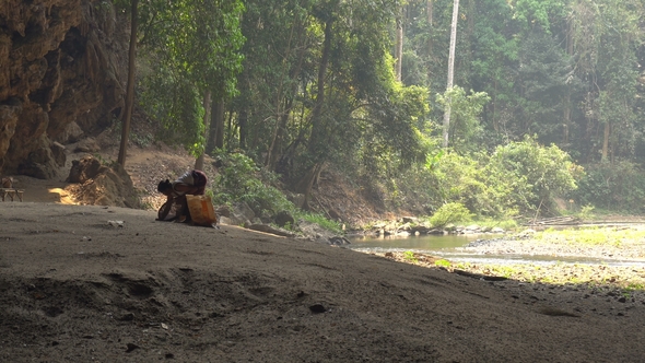 Older Woman Is Collecting Bat Guano on the Bottom of Big Cave with River Flowing From the Bowels