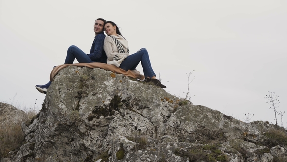 Lovely Couple Resting in Embraces on the Top of Rock in Windy Day.