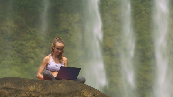Lady Sits on Rock Poses at Laptop by Foamy Water Falling