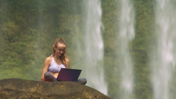 Wind Shakes Hair Girl Works on Notebook by Waterfall