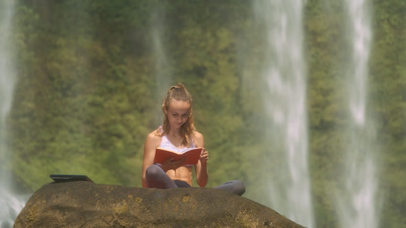 Girl Reads Book against Plants behind Waterfall Jets