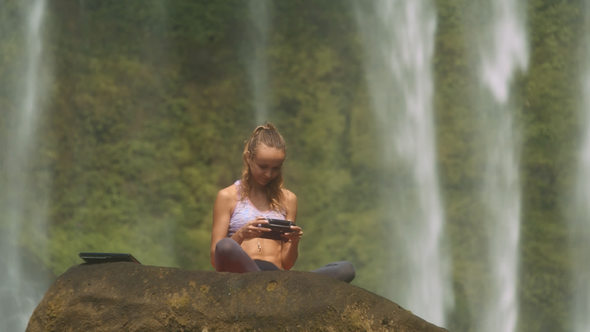 Woman Watches Video on Tablet against Waterfall