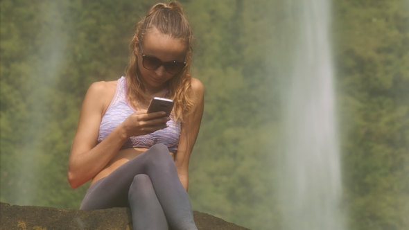 Nice Girl in Sunglasses Reads Sms near Waterfall