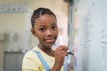 board. Portrait of black schoolgirl doing math addition at whiteboard in classroom. Closeup face of schoolgirl looking at camera after solving mathematical operation.