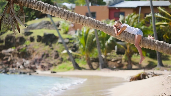 Adorable Little Girl Sitting on Palm Tree During Summer Vacation on White Beach