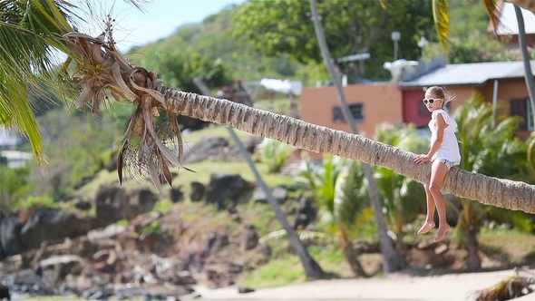 Adorable Little Girl Sitting on Palm Tree During Summer Vacation on White Beach