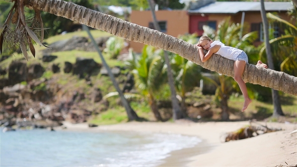 Adorable Little Girl Sitting on Palm Tree During Summer Vacation on White Beach