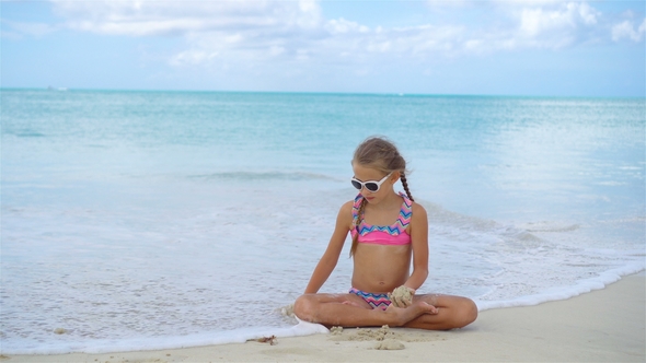 Adorable Active Little Girl Sitting on Sandy Beach