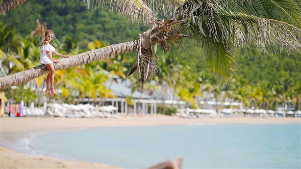 Adorable Little Girl Sitting on Palm Tree During Summer Vacation on White Beach