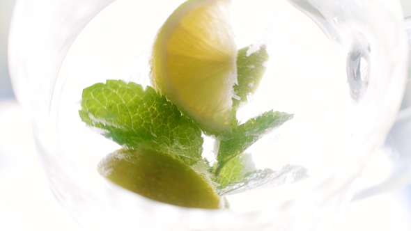 View From Top on Lemon Slices, Ice Cubes and Leaves of Mint Rotating and Floating in Big Glass