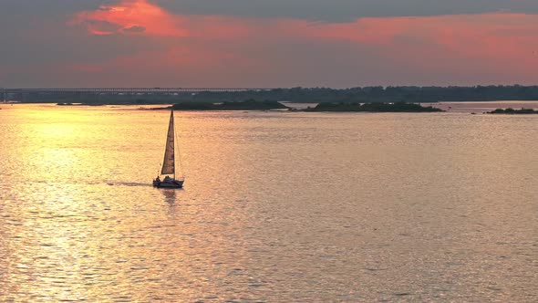 Sports Sailboat Goes Along Volga River Against Background of Colorful Orange Sunset with Cirrus