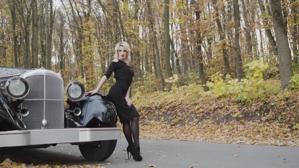 Portrait of Passionate Blonde Stands in Sexy Pose at Retro Cabriolet in Forest
