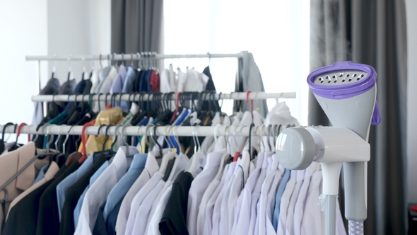 Steam Iron Steaming with a Lot of Clothes on Hanger in the Background