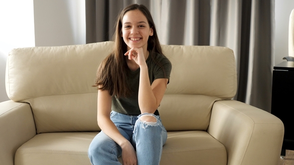Young Teenage Girl Is Sitting on the Couch and Smiles Naturaly To the Camera