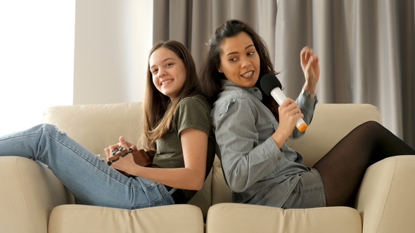 Happy and Positive Sisters Playing and Singing on the Sofa