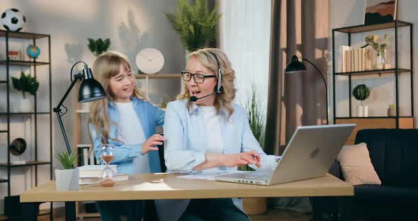 Woman in Headset Working at Home on Computer when Her Playful Active Daughter Running Up