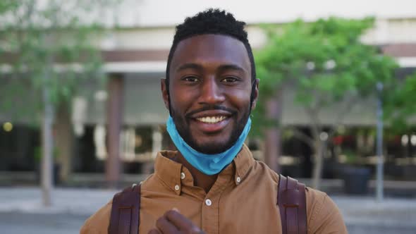 Portrait of smiling african american businessman with face mask in urban park