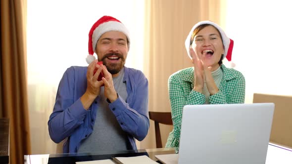 A Couple Sits at a Table Wearing Christmas Hats and a Gift Box Arrives for Them