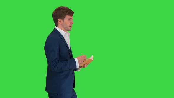 Thinking Businessman Writing Notes in His Notebook While Walking on a Green Screen, Chroma Key.