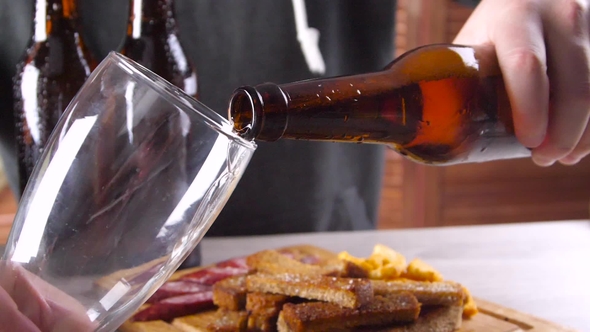 Man at the Table with Beer Snacks Pours Beer Into a Glass