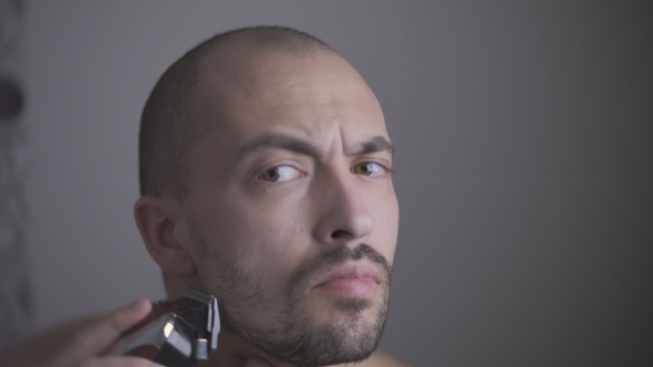 Young Caucasian Man Dry Shaving His Beard with an Electric Trimmer