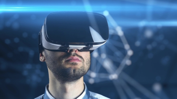 A Young Man with a Beard in Glasses of Virtual Reality on a Technological Background alt