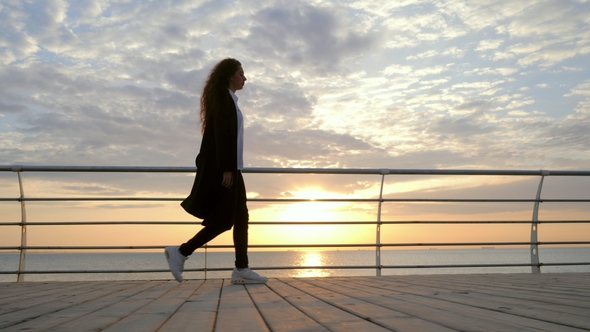Silhouette of Young Stylish Business Woman with Curly Hair Are Walking Along the Wooden Embankment