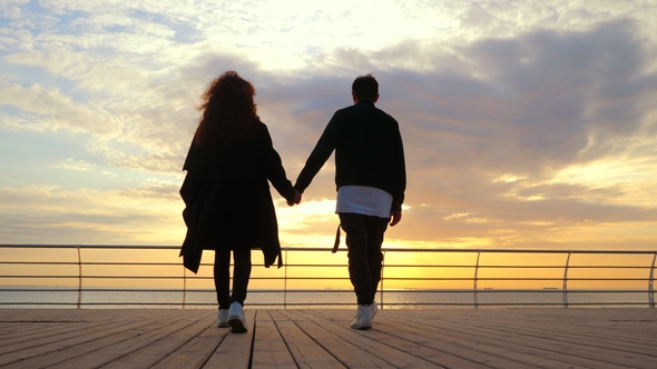 Young Happy Couple in Love. Pair Holding Hands and Walking on Wooden Pier Near Sea or Ocean. People