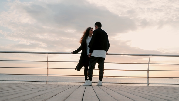 Young Happy Couple in Love. Pair Standing on Wooden Pier Near Sea or Ocean and Smiling To Each Other