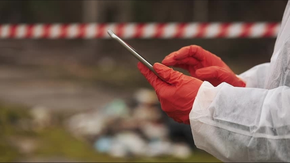 Man in Bio-hazard Suit and Gas Mask Takes Notes in His Tablet Standing on the Polluted Land