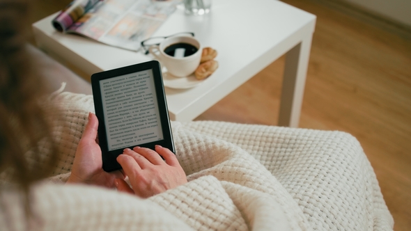EBook on E-Reader in Hands of Adult Woman Sitting in a Cozy Room