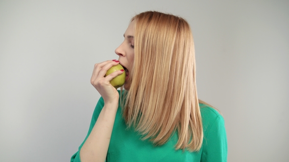 Portrait of Blonde Woman Eating Green Apple. Young Woman Propose To Bite Apple