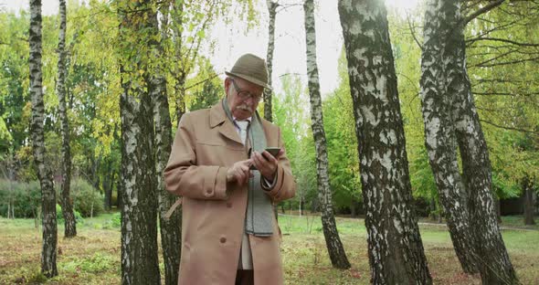 Elegant Old Man Typing on Smartphone at Camera in Beautiful Birch Park