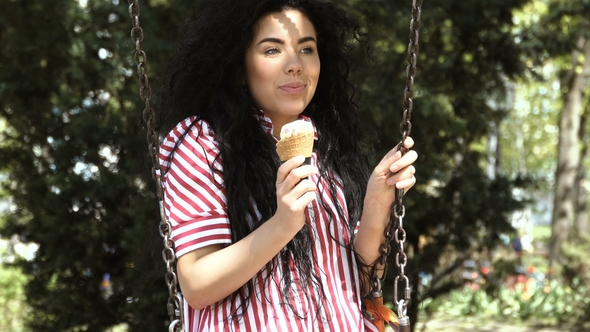 Beautiful Brunette Eat Ice Cream on a Swing in Park