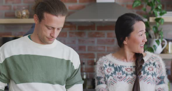 Three happy diverse female and male friends talking while cooking together in kitchen