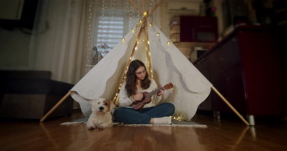 The Girl Sits in a Children's Tent with a Dog Jack Russell and Plays the Guitar
